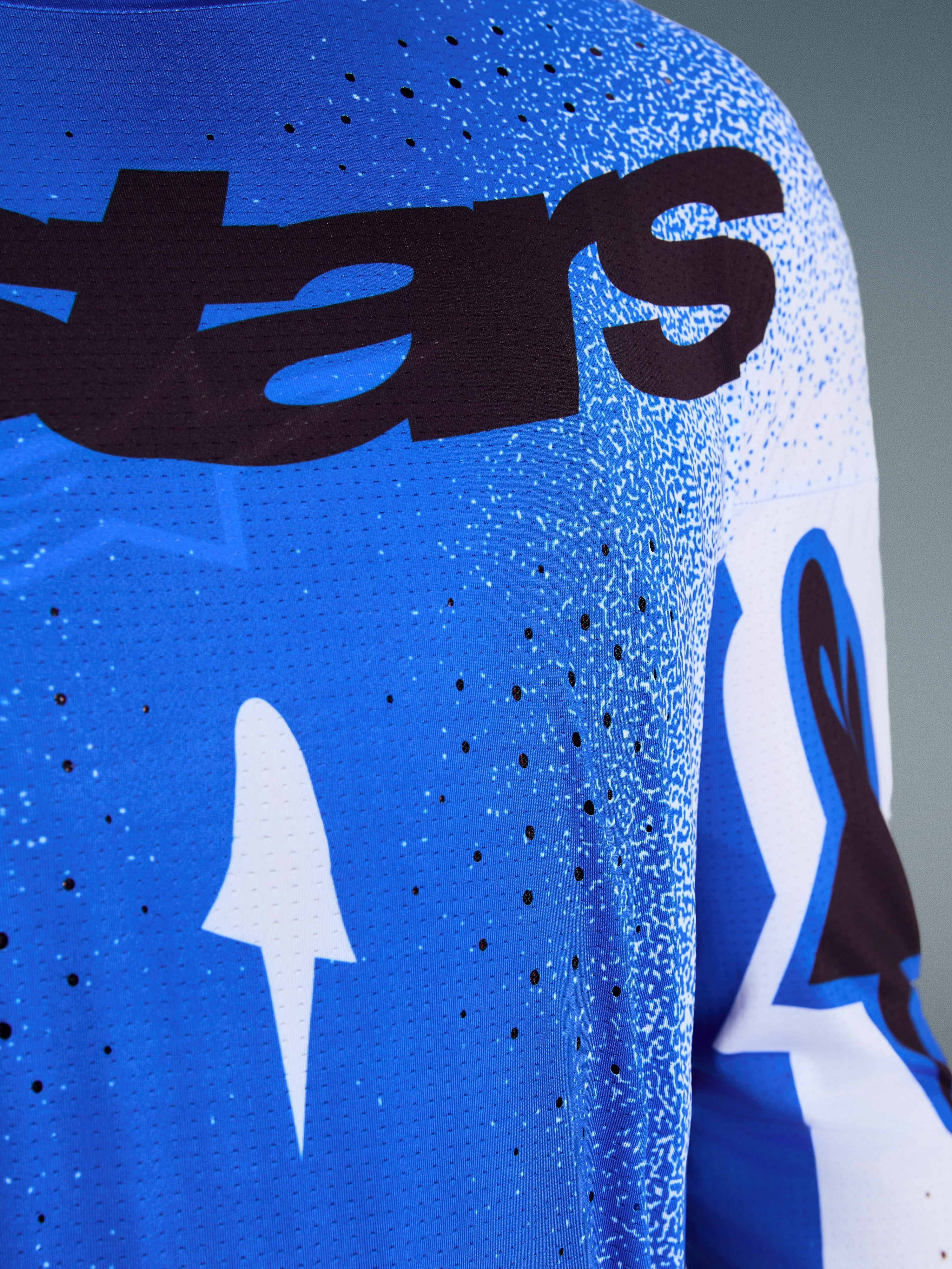Alpinestars 2026 Supertech Scenz Jersey, close-up of Ucla Blue and White design, featuring laser-cut perforations for ventilation, black 'stars' branding, and breathable mesh fabric for professional motocross racing.