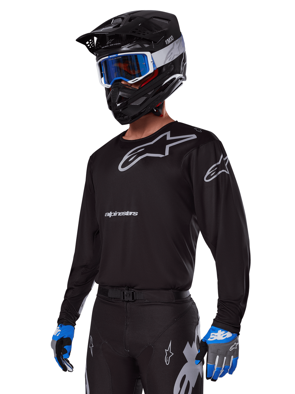Motocrossförare i Alpinestars 2025 Racer Graphite-utrustningsset, svart tröja med grå Alpinestars-logotyper, matchande svarta byxor med grå detaljer, svart hjälm med blå och vita goggles, blå och grå handskar, teknisk outfit för terrängkörning