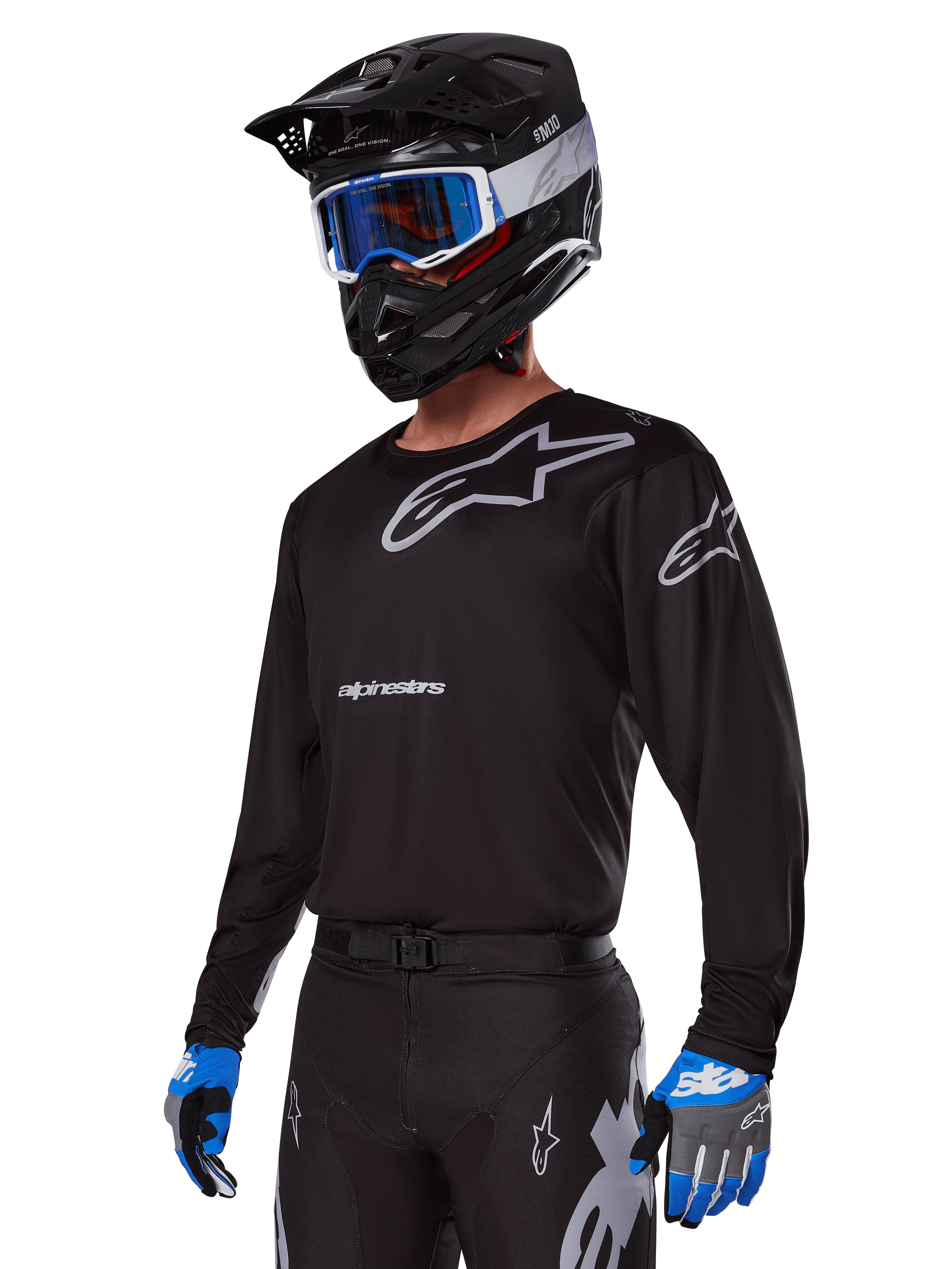 Motocrossförare i Alpinestars 2025 Racer Graphite-utrustningsset, svart tröja med grå Alpinestars-logotyper, matchande svarta byxor med grå detaljer, svart hjälm med blå och vita goggles, blå och grå handskar, teknisk outfit för terrängkörning