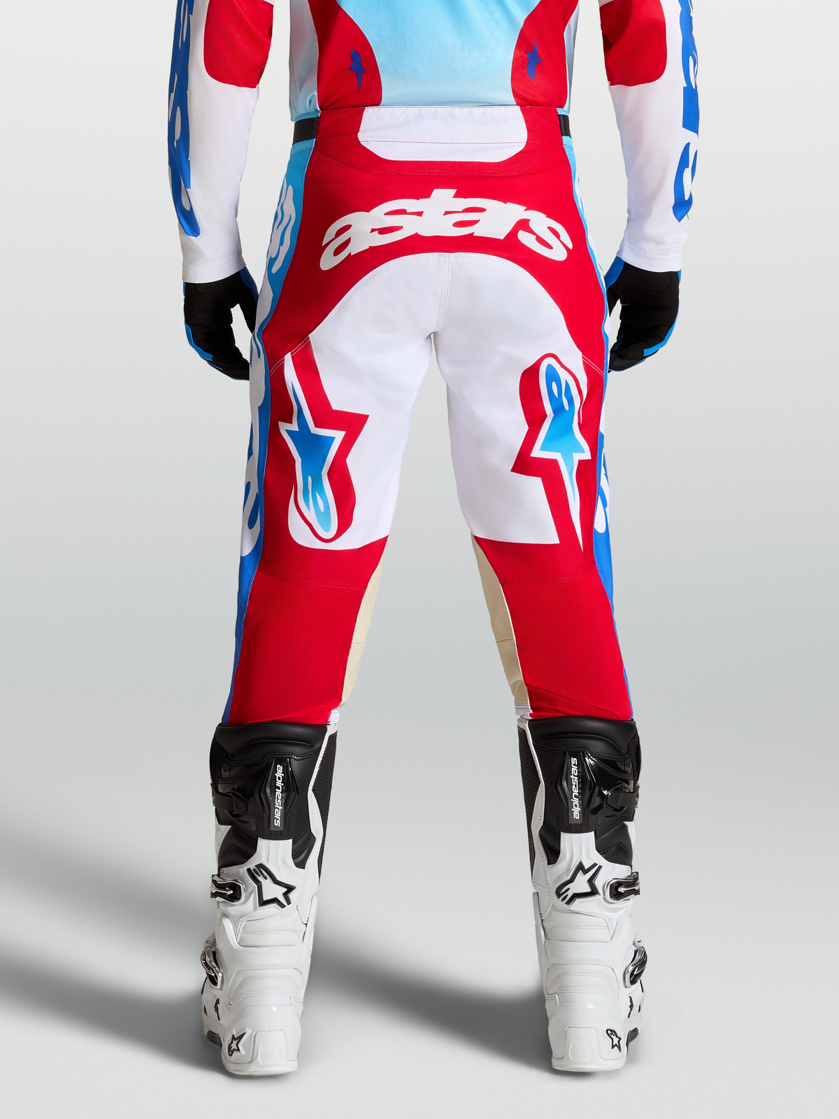 Alpinestars Racer Hunt Pants, red and white motocross pants shown from the rear on a rider, featuring light blue accents and ergonomic pre-curved leg construction.