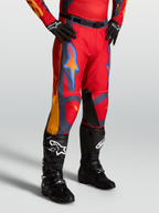 Alpinestars Racer Hunt byxor, röd motocrossbyxor för herr med gråa och korallfärgade detaljer, bärs med svarta stövlar och handskar.