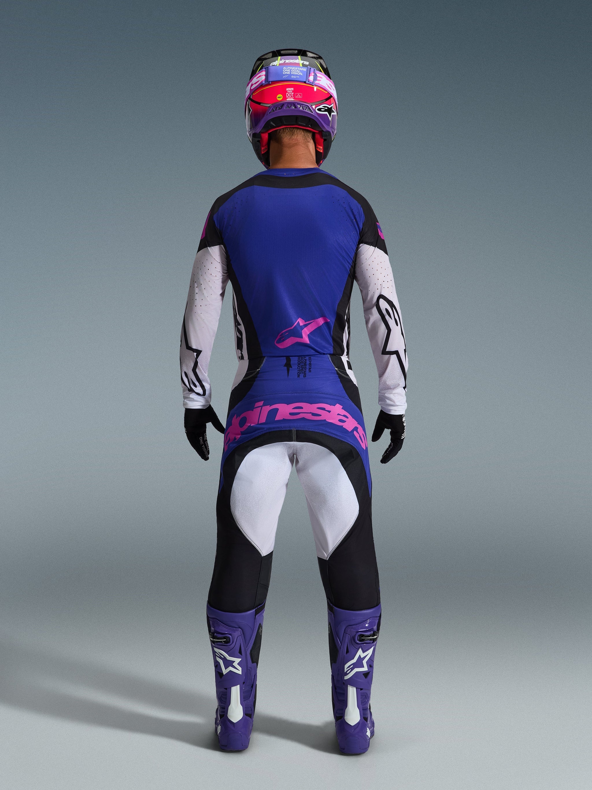 Motocrossförare sedd bakifrån klädd i 2026 Techstar Knif Jersey, svart, ljusgrå och lila, matchande motocrossbyxor med rosa logotyp, lila stövlar och hjälm, koordinerad högpresterande terrängutrustning
