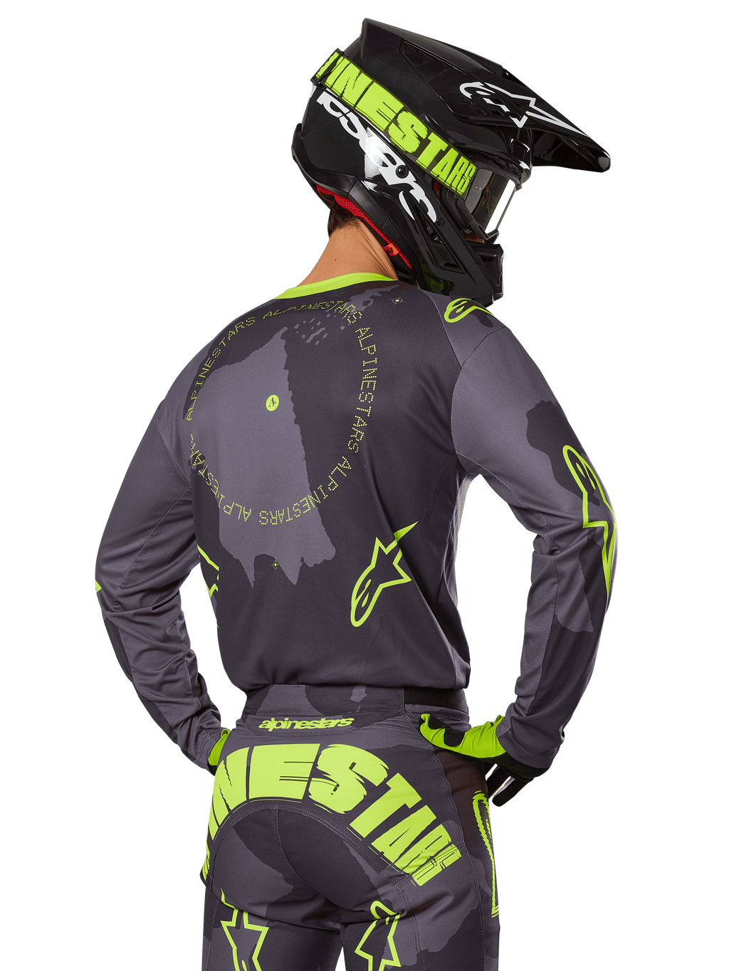Motocrossförare sedd bakifrån i 2025 Racer Hollow Gear Set, grå tröja med fluorescerande gul cirkulär text och stjärnlogotyper, matchande grå och gula byxor med tydlig logotyp över sätet, svart och limegrön hjälm, koordinerad outfit för terrängkörning