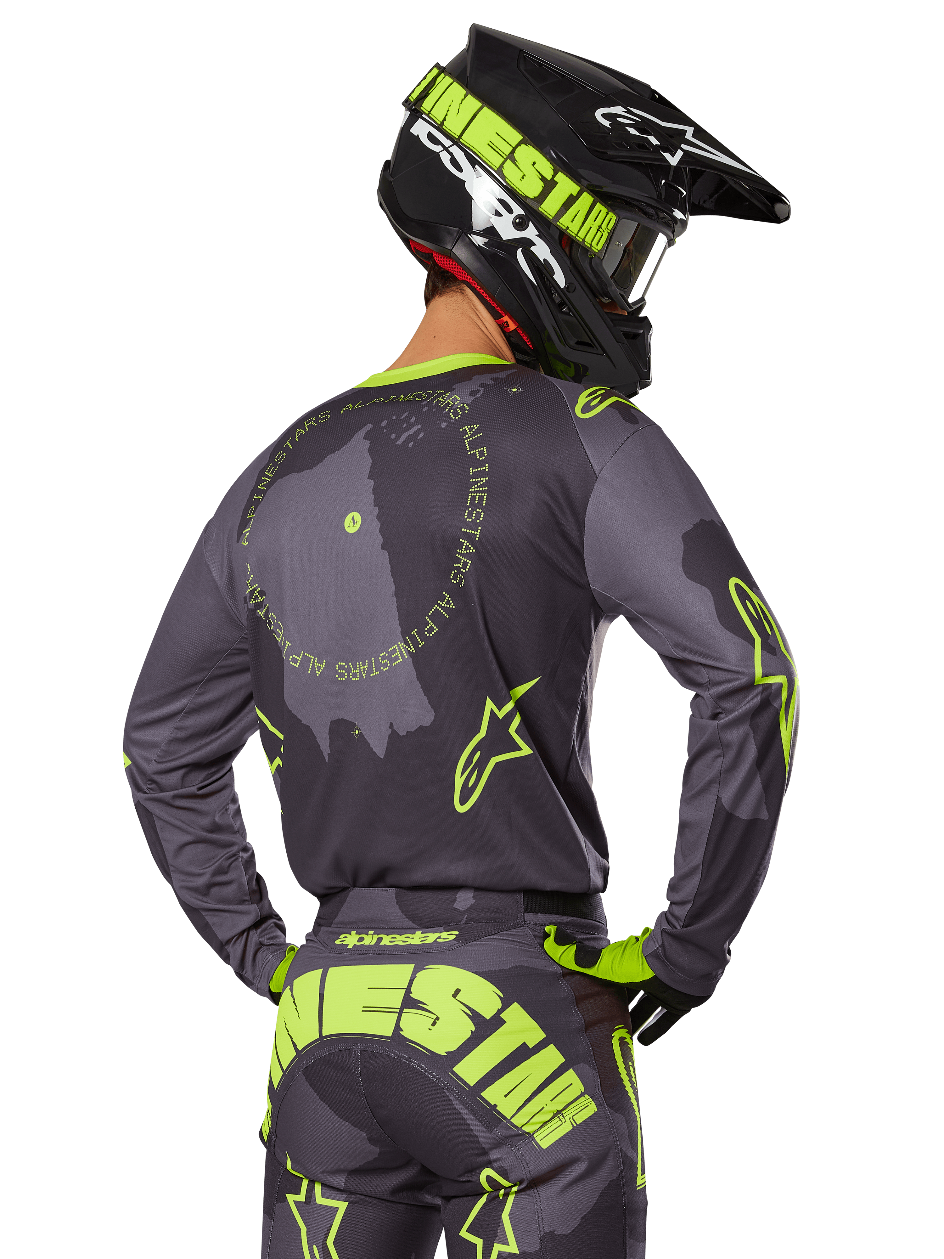 Motocrossförare sedd bakifrån i 2025 Racer Hollow Gear Set, grå tröja med fluorescerande gul cirkulär text och stjärnlogotyper, matchande grå och gula byxor med tydlig logotyp över sätet, svart och limegrön hjälm, koordinerad outfit för terrängkörning