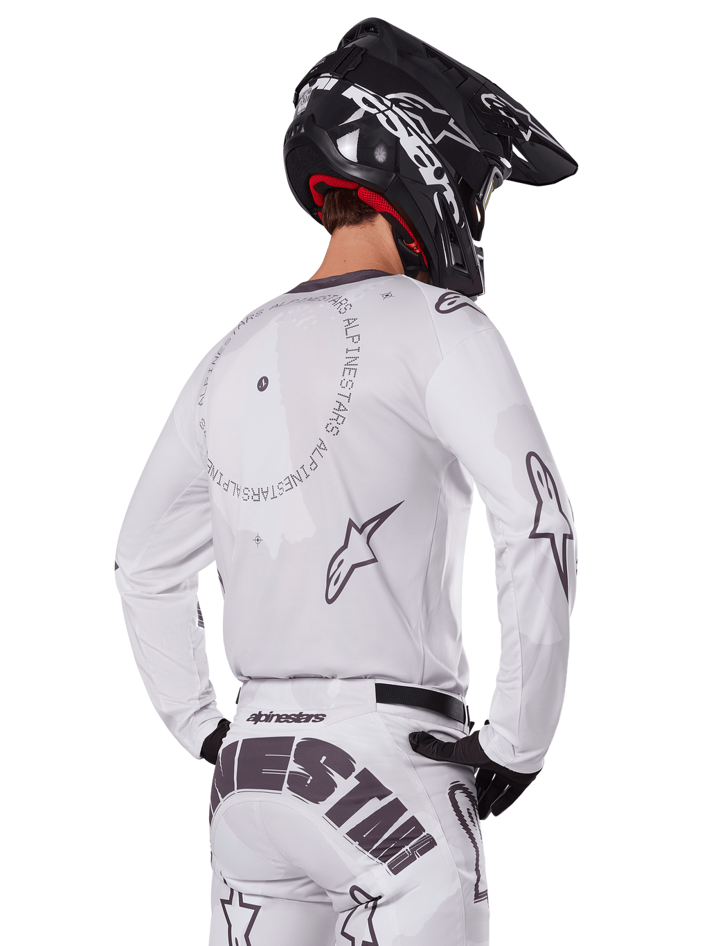 Motocross rider from the back wearing the Alpinestars 2025 Racer Hollow Gear Set in White, white long-sleeve jersey with grey star logos and circular graphics, matching white pants with bold branding on the seat, black helmet, coordinated off-road racing gear.