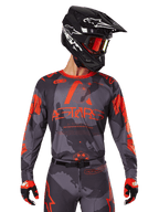 Alpinestars 2025 Racer Hollow Jersey, Motocross Jersey, Gray Camo and Orange Fluo, worn with matching gear set including pants and gloves, featuring a black helmet with white graphics and goggles, bold ASTARS branding, protective off-road racing sportswear