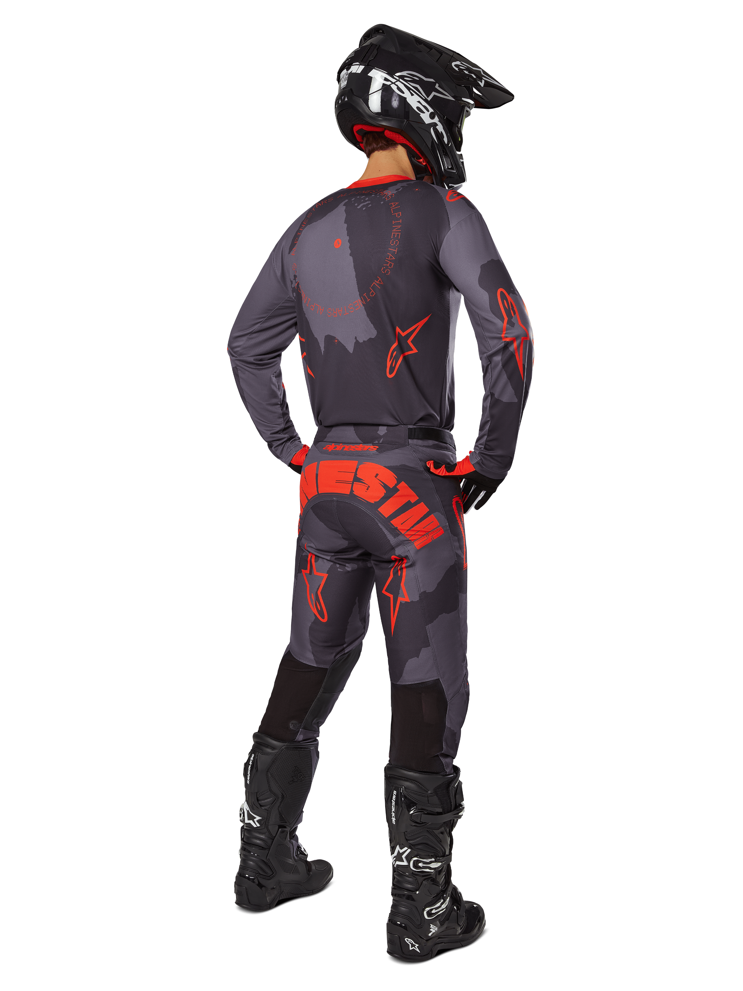 Motocross rider from a rear view wearing the Alpinestars 2025 Racer Hollow Jersey in Gray Camo Orange Fluo, matching camo pants with orange Alpinestars text, black helmet, and black boots, coordinated gear set for off-road riding