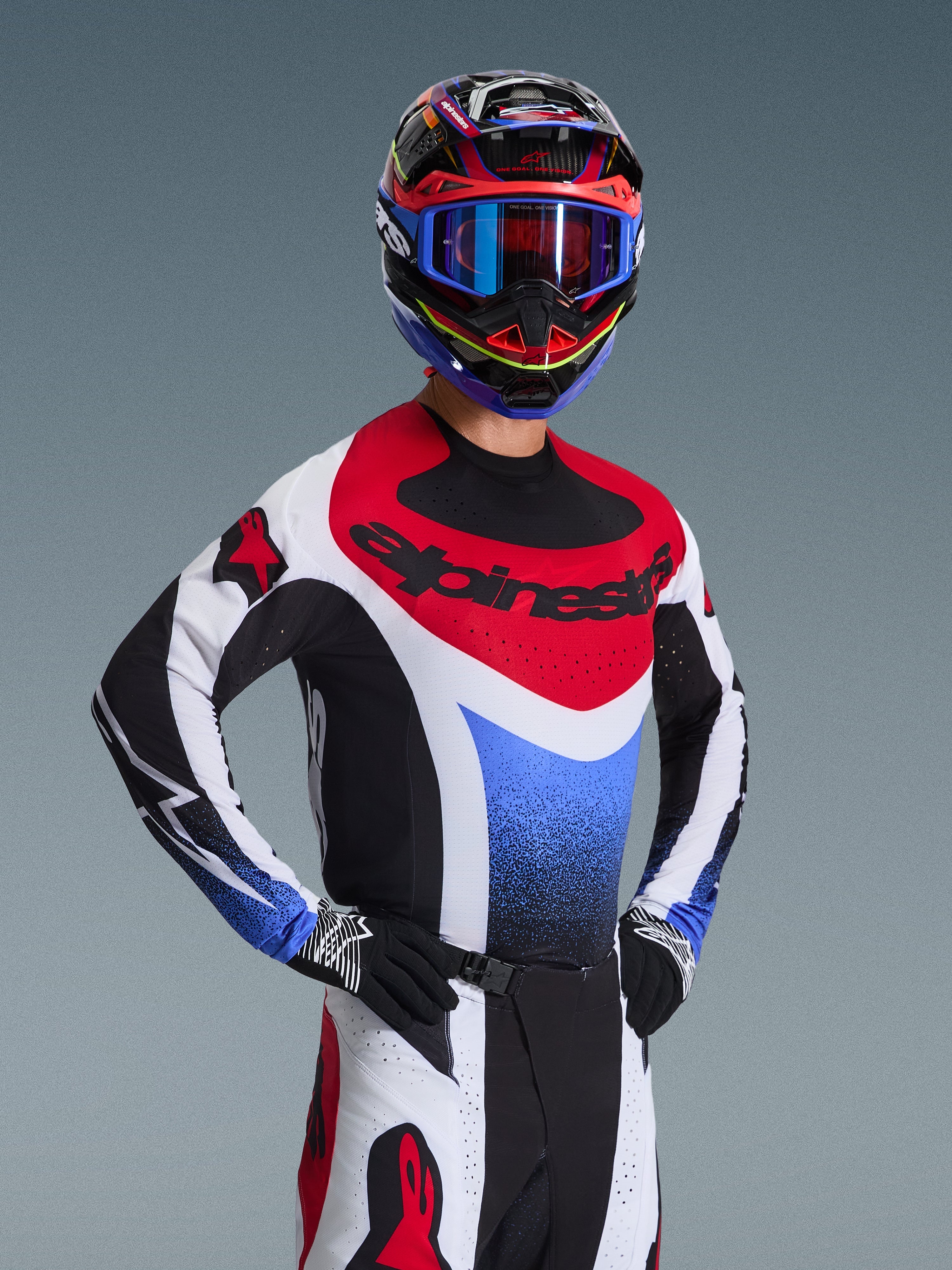 Alpinestars 2026 Techstar Knif utrustningsset, motocrossförare i en röd, vit och blå racingtröja med svarta detaljer, matchande flerfärgad hjälm och goggles, svarta handskar, professionell utrustning för motocrosstävling.