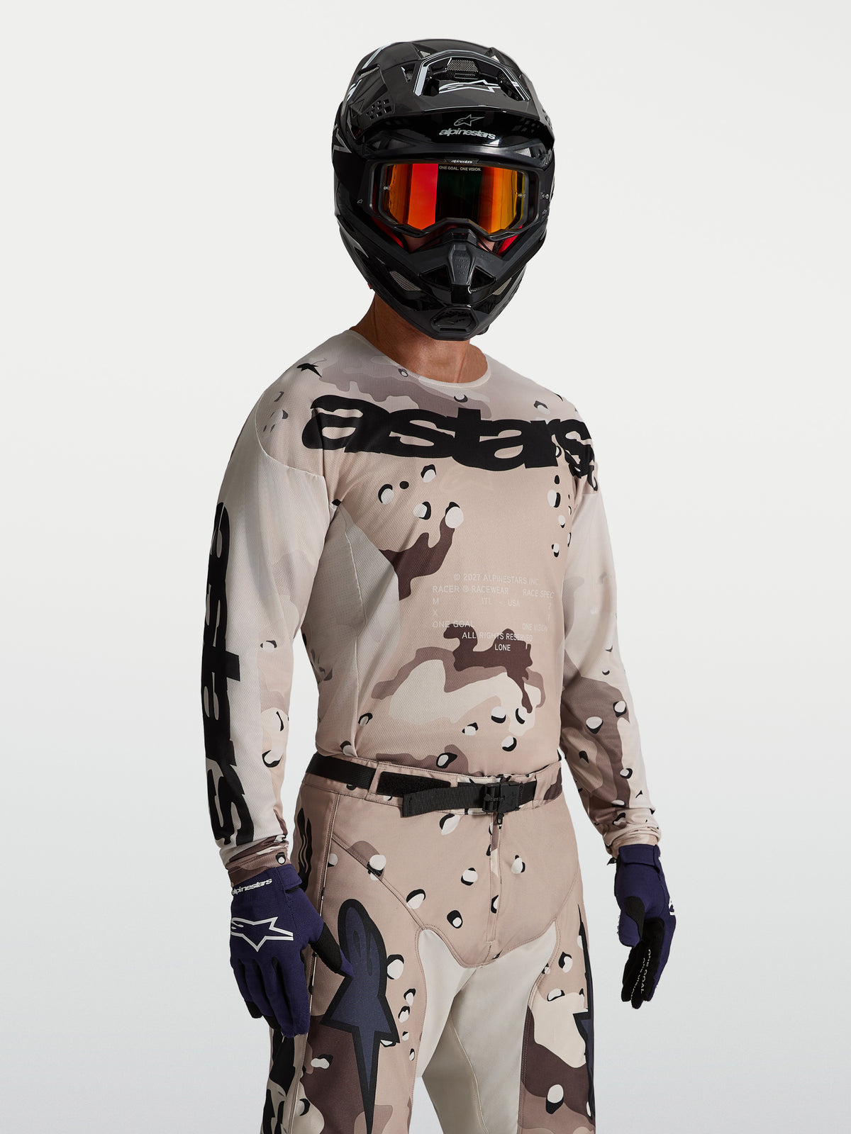 Alpinestars Racer Lone tröja, motocrosströja för herr i ökenkamouflage tan och svart, fukttransporterande polytyg med tävlingspassform, bärs av modell med matchande utrustning för terrängkörning.