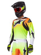 Motocross rider wearing Alpinestars 2025 Fluid Wurx Gear Set, Yellow and Orange gradient jersey with black accents and large star logos, matching motocross pants, black full-face helmet with red-tinted goggles, and yellow gloves, coordinated high-performance outfit for off-road racing