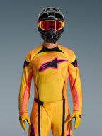 2026 Techstar Nomur-tröja i Orange Yellow Pink, buren av en motocrossförare med en matchande svart hjälm och rosa goggles, med en stor rosa Alpinestars-logotyp på bröstet, atletisk racingpassform för terrängprestanda.