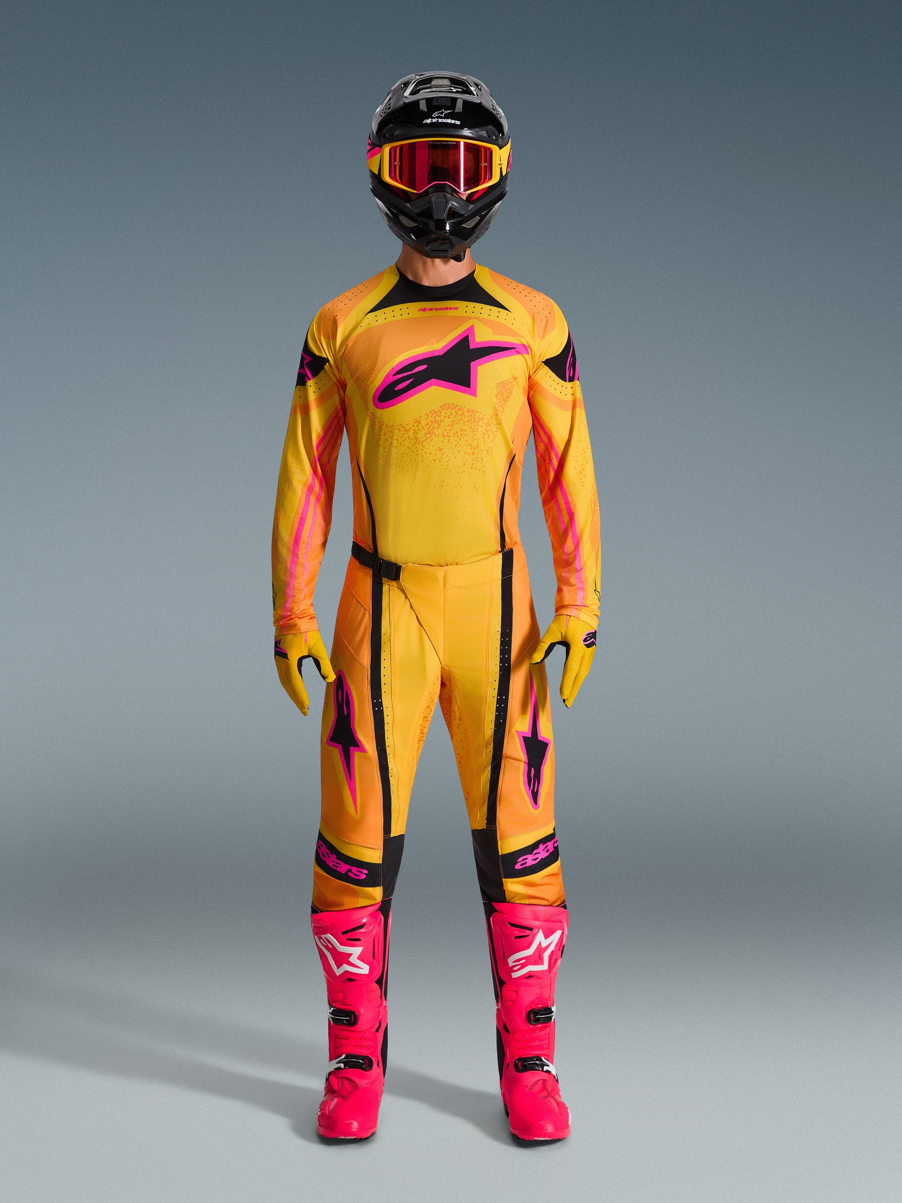 Motocrossförare iförd 2026 Techstar Nomur-tröja i orange, gult och rosa, matchad med tillhörande motocrossbyxor, svart hjälm med rosa goggles och färgstarka rosa stövlar, atletisk race-fit-utrustning för terrängtävling