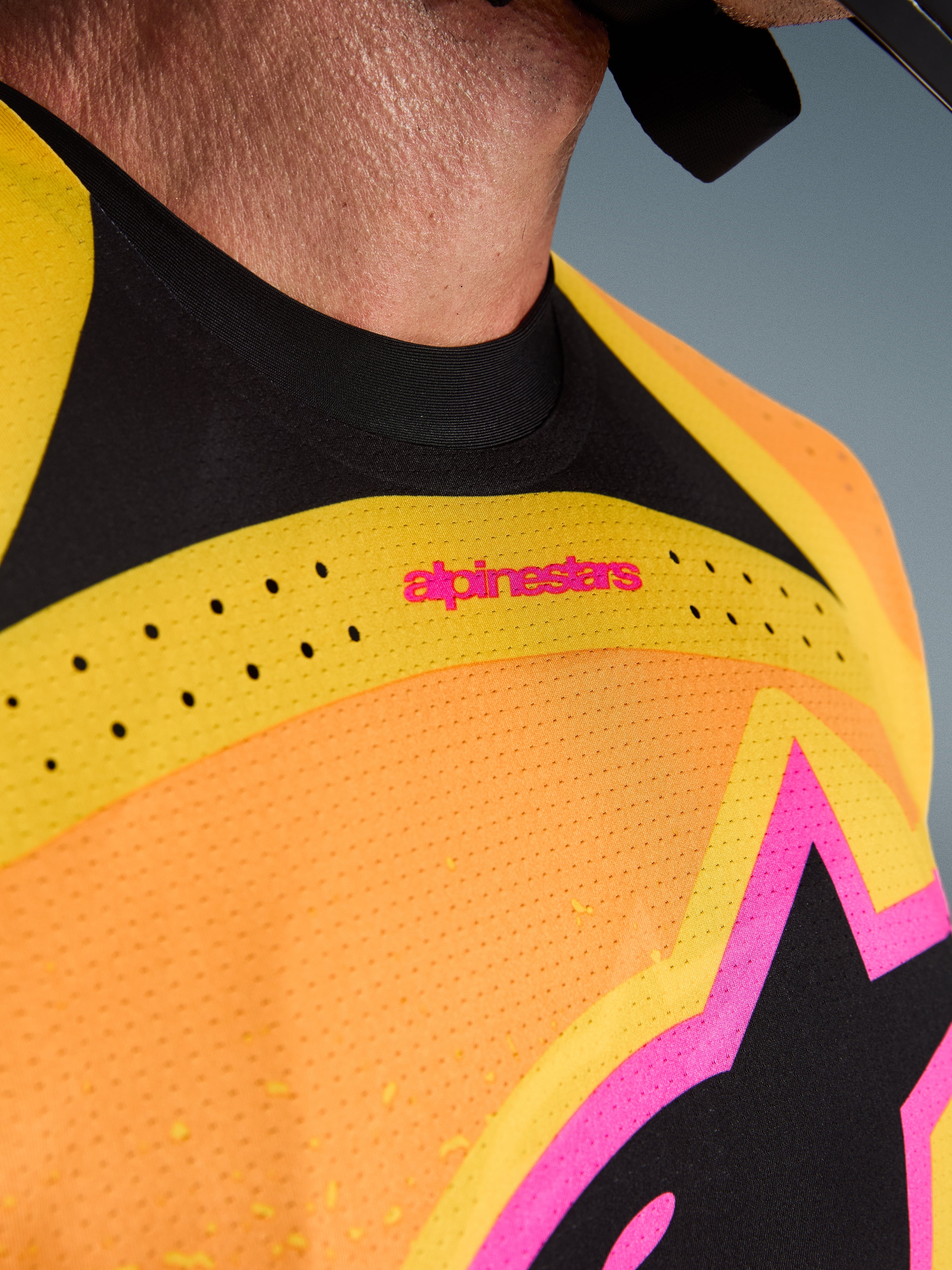 Alpinestars 2026 Techstar Nomur-tröja, motocrosströja, orange, gul och rosa, närbild på bröst och krage, med laserskuren ventilation, rosa logotyp och ventilerande meshtyg