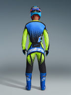 Ryggvy av en motocrossförare klädd i 2026 Techstar Nomur Jersey i Dark Navy, Yellow Fluo och UCLA Blue, matchande gula och svarta motocrossbyxor med 'Astars'-logotyp, blå racingstövlar och en matchande hjälm, komplett professionell utrustning för terrängkörning.