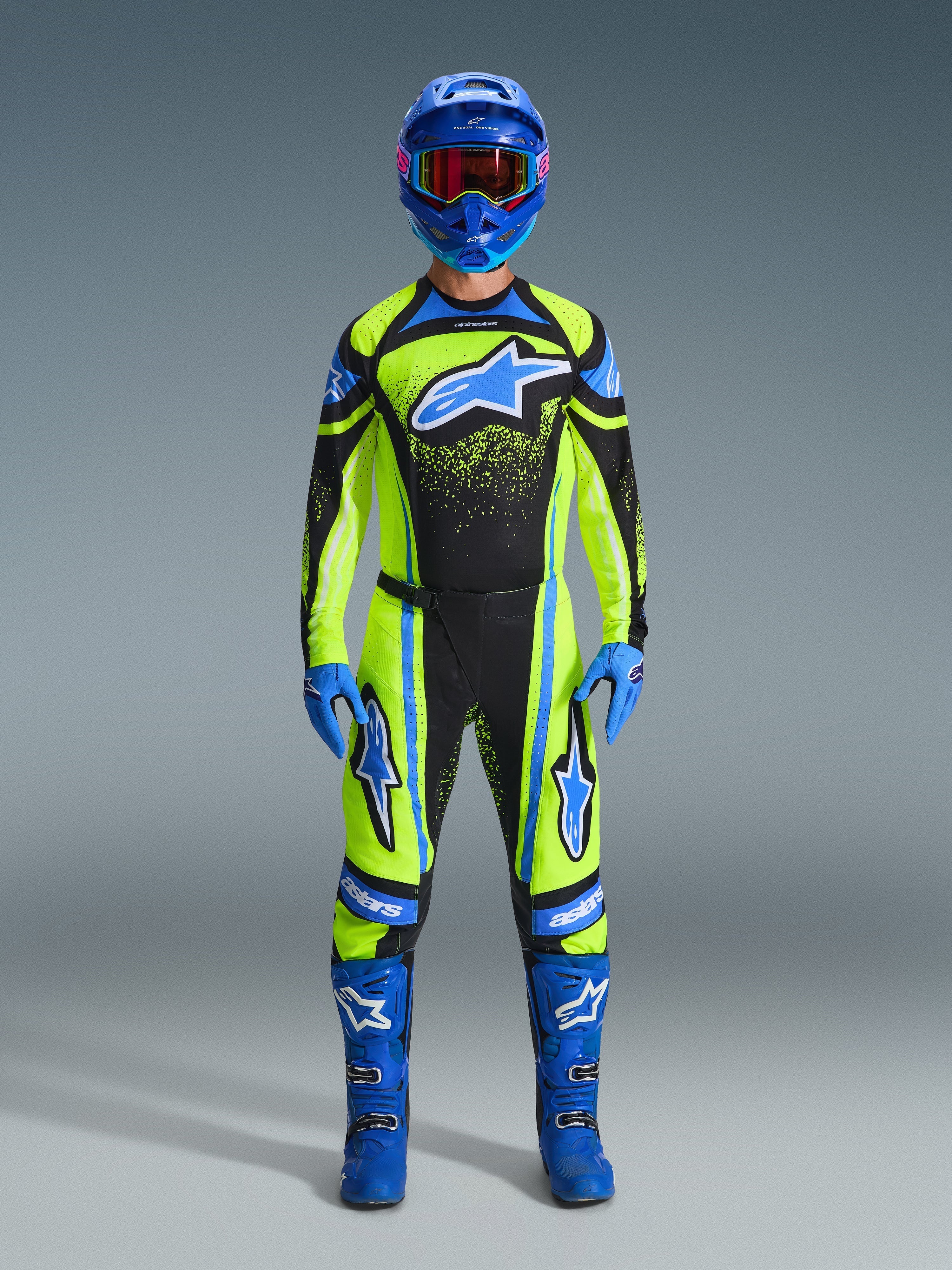 Motocrossförare iklädd komplett racingutrustning, 2026 Techstar Nomur-tröja i gul fluo och mörk marinblå, matchande motocrossbyxor, blå hjälm med rödfärgade goggles, blå handskar och blå stövlar, koordinerad professionell outfit för terrängkörning