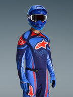 Motocrossförare i Alpinestars 2026 Techstar Nomur-tröja, racingutrustning i färgerna Dark Navy, orange och UCLA Blue, med en stor orange Astars-logotyp, matchande blå hjälm och handskar, atletisk tävlingsoutfit för terrängkörning.