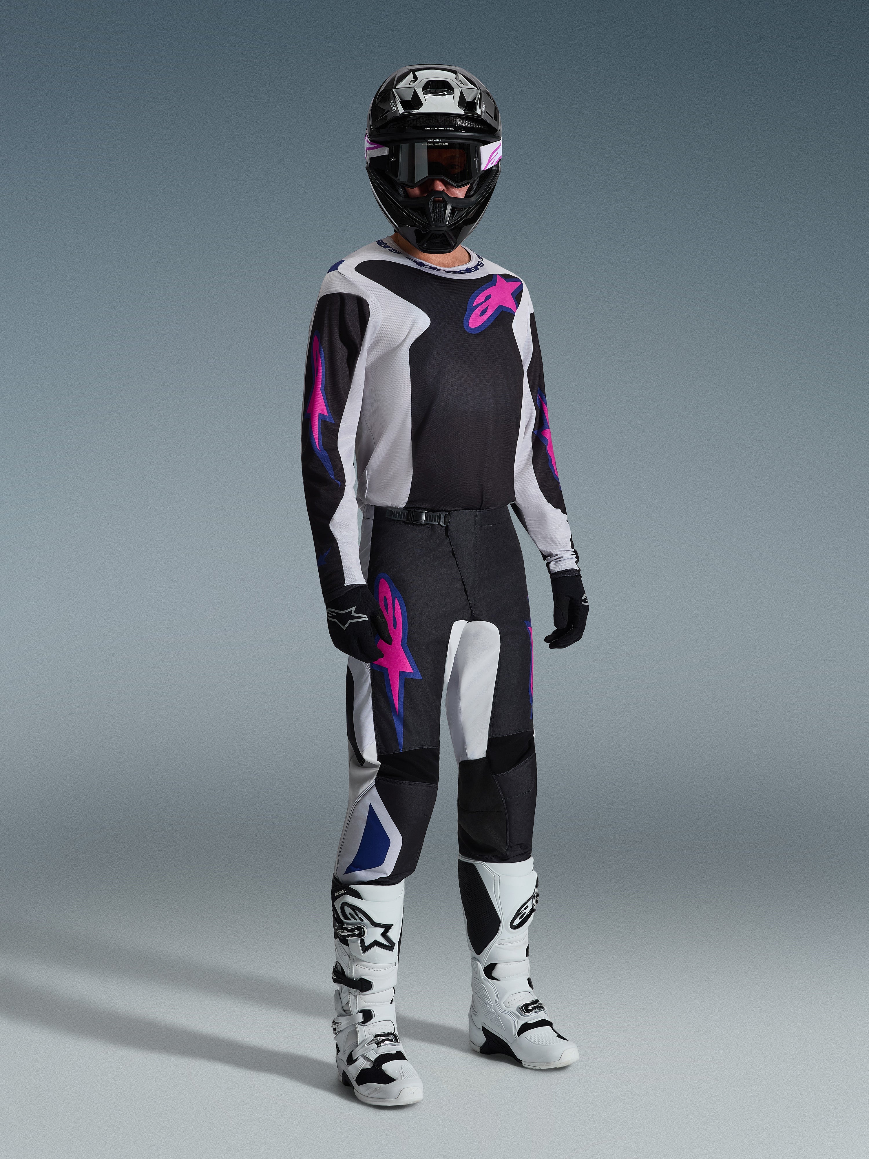Alpinestars 2026 Fluid Grid Gear Set, motocross rider wearing black and white jersey and pants with pink and blue accents, black helmet, black gloves, and white boots, complete racing ensemble on a gray background