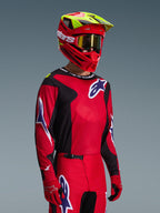 Motocrossförare iklädd Alpinestars 2026 Fluid Grid-utrustningsset, röd och svart tröja med vita och blå logotypdetaljer, matchande röda och svarta byxor, röd hjälm med gula detaljer och guldiga goggles, koordinerad offroad-racingutrustning