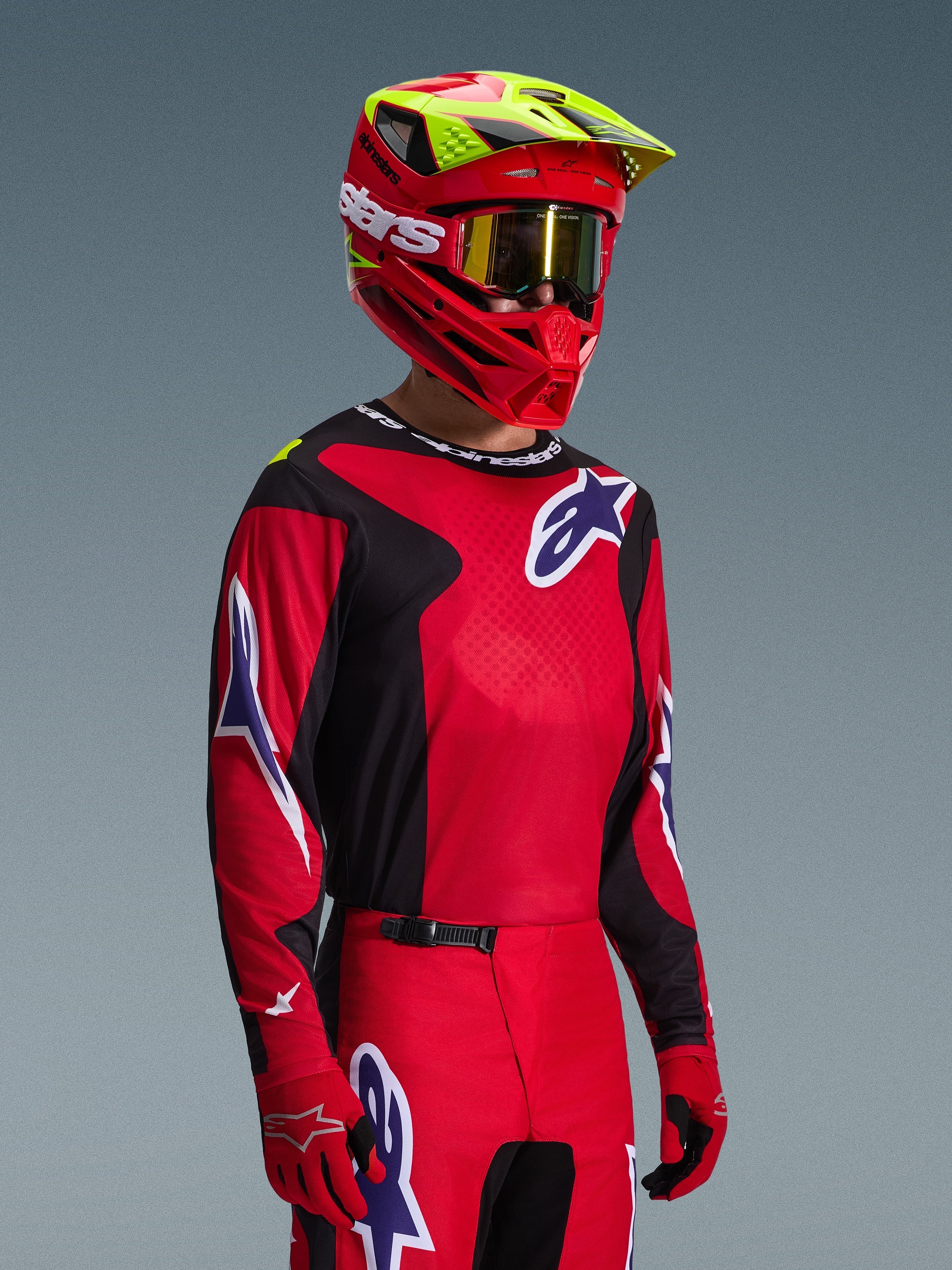 Motocrossförare iklädd Alpinestars 2026 Fluid Grid-utrustningsset, röd och svart tröja med vita och blå logotypdetaljer, matchande röda och svarta byxor, röd hjälm med gula detaljer och guldiga goggles, koordinerad offroad-racingutrustning
