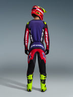 Motocrossförare sedd bakifrån bärande Alpinestars 2026 Fluid Grid Gear Set i färgen Red Black Purple, med lila ryggpanel och röda ärmar på tröjan, matchande röda och svarta byxor, neongula motocross-stövlar och en röd och neongul hjälm.