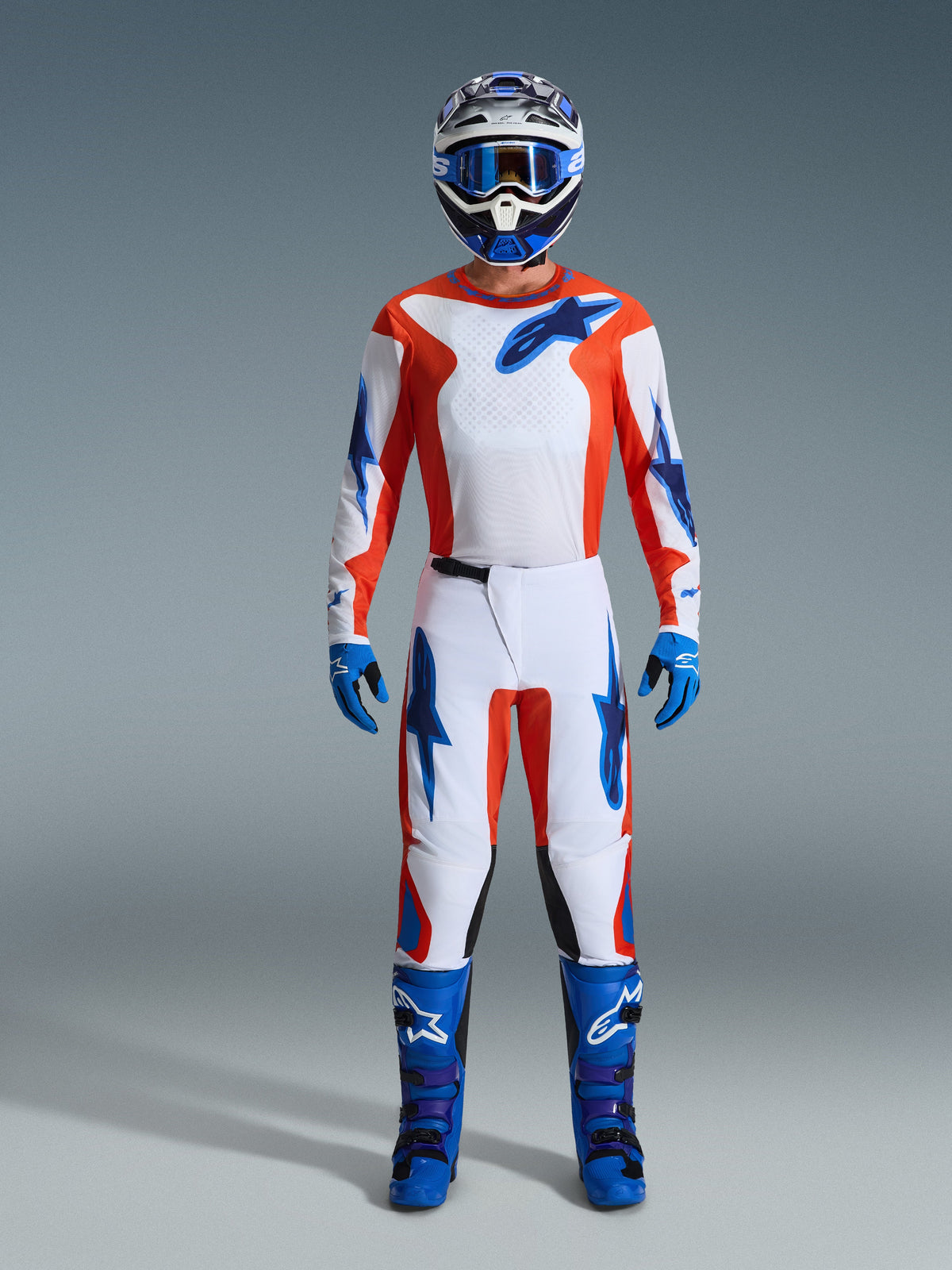Alpinestars 2026 Fluid Grid Gear Set, motocrossförare i komplett utrustning, vit tröja och byxor med orange och UCLA-blå detaljer, matchande blå och vit hjälm med blå goggles, blå handskar och blå motocross-stövlar, koordinerad racingoutfit för terrängkörning