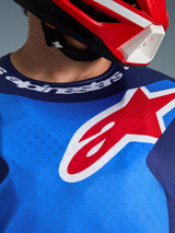 Alpinestars 2026 Fluid Grid tröja, blå och röd, närbild av bröstet och sportkragen, stor röd och vit Alpinestars stjärnlogotyp, Alpinestars-detaljer vid halsringningen, bärs med en röd och vit hjälm