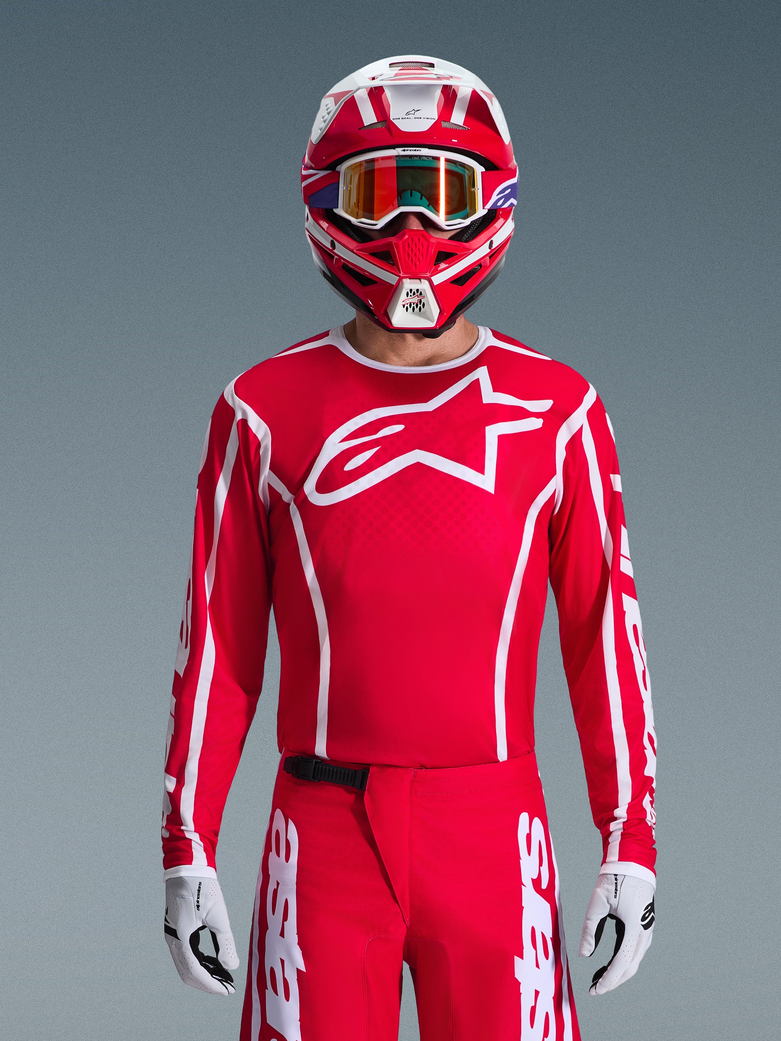 Motocrossförare i komplett Alpinestars 2026 Fluid Apex-utrustningsset, röd tröja med stor vit stjärnlogotyp på bröstet, matchande röda byxor med vita logotyper, röd och vit hjälm med iriserande goggles, vita och svarta handskar, koordinerad röd och vit outfit för terrängkörning