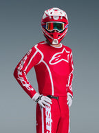 Motocrossförare som bär Alpinestars 2026 Fluid Apex utrustningsset i rött och vitt, med en röd tröja med vita logotyper, matchande byxor, vita handskar och en röd och vit hjälm med iriserande goggles, koordinerad outfit för terrängkörning