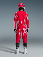 Vy bakifrån av en motocrossförare iklädd Alpinestars 2026 Fluid Apex-utrustningsset, klarröd tröja och byxor med vita ränder och logotyper, vita och svarta stövlar och en röd hjälm, professionell racingutrustning för terrängkörning