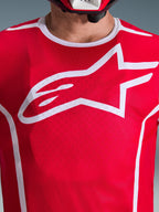 Närbild av Alpinestars 2026 Fluid Apex-tröja i rött och vitt, med en stor vit Astars-logotyp på bröstet, ventilerande konstruktion i polytextil-mesh och vit kragkant, motocrosskläder