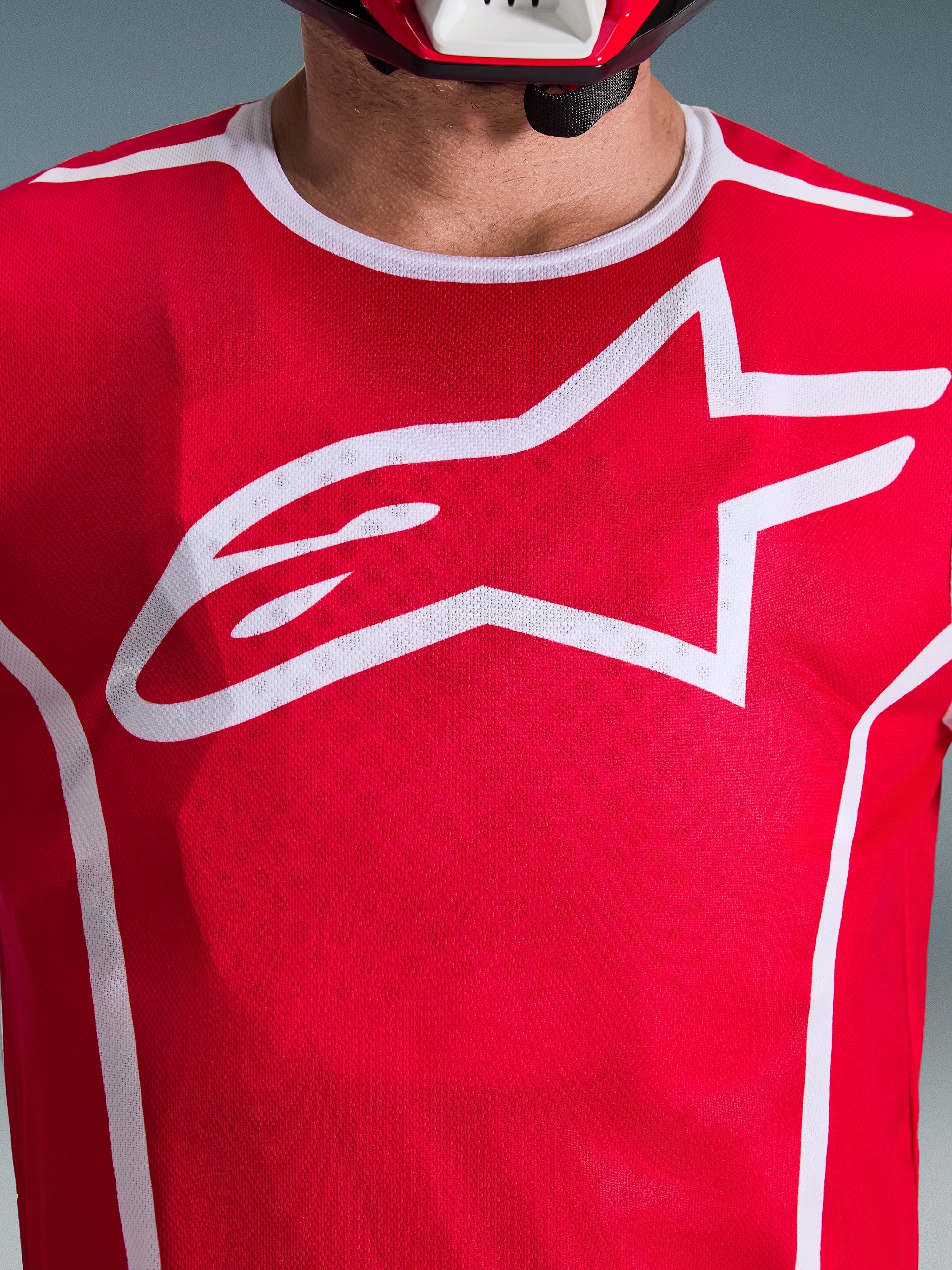 Närbild av Alpinestars 2026 Fluid Apex-tröja i rött och vitt, med en stor vit Astars-logotyp på bröstet, ventilerande konstruktion i polytextil-mesh och vit kragkant, motocrosskläder