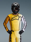 Alpinestars 2026 Fluid Apex tröja, motocrosströja, gul och svart med en vit ärm och stor svart logotyp på bröstet, bärs som en del av en komplett racingutrustning med matchande byxor, svart hjälm och handskar