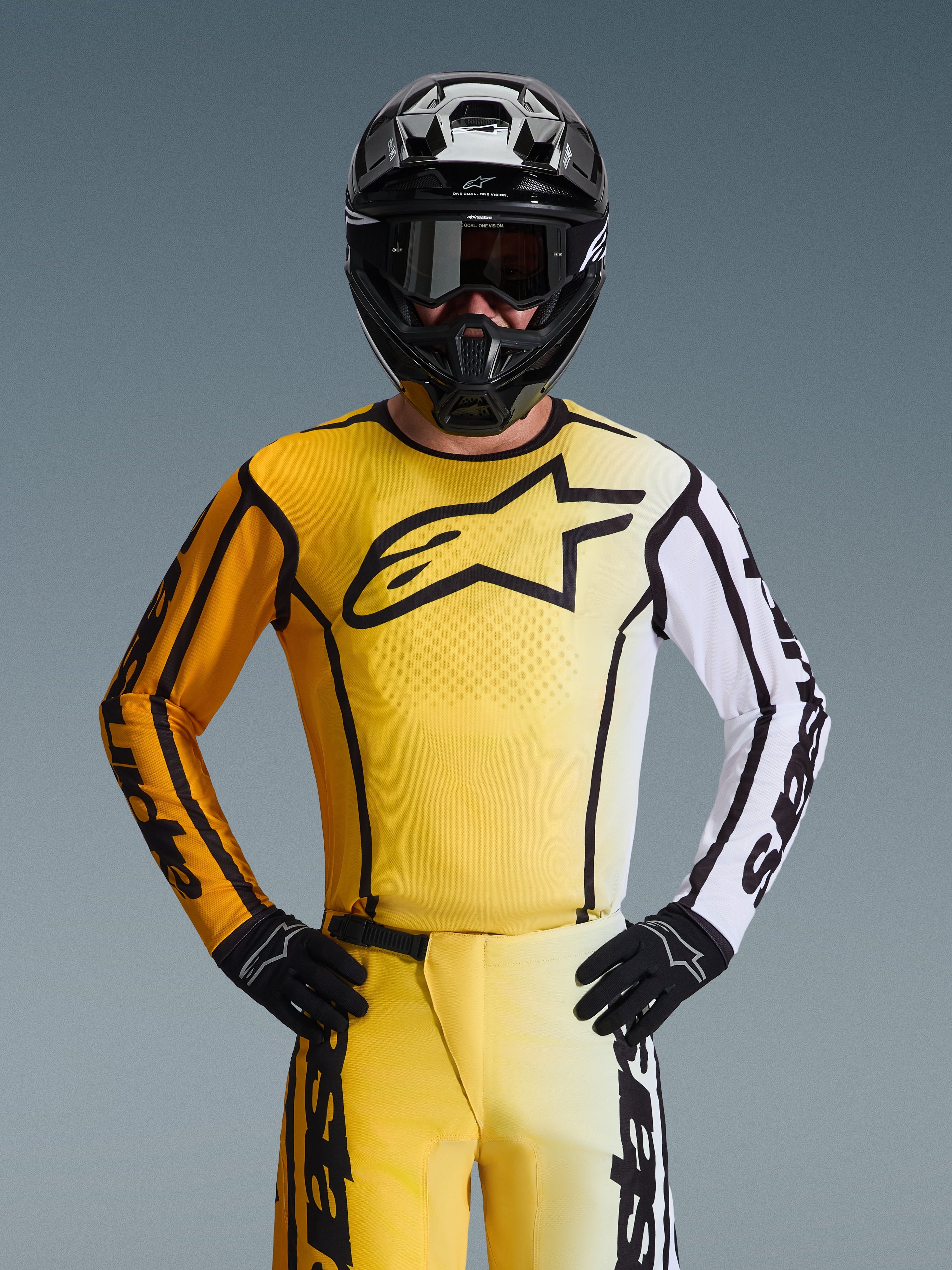 Alpinestars 2026 Fluid Apex tröja, motocrosströja, gul och svart med en vit ärm och stor svart logotyp på bröstet, bärs som en del av en komplett racingutrustning med matchande byxor, svart hjälm och handskar
