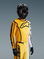 Alpinestars 2026 Fluid Apex tröja, motocrosströja, gul och svart med vita detaljer, bärs av en förare med svart hjälm och goggles, stor svart stjärnlogotyp på bröstet, matchande racingutrustning för terrängkörning
