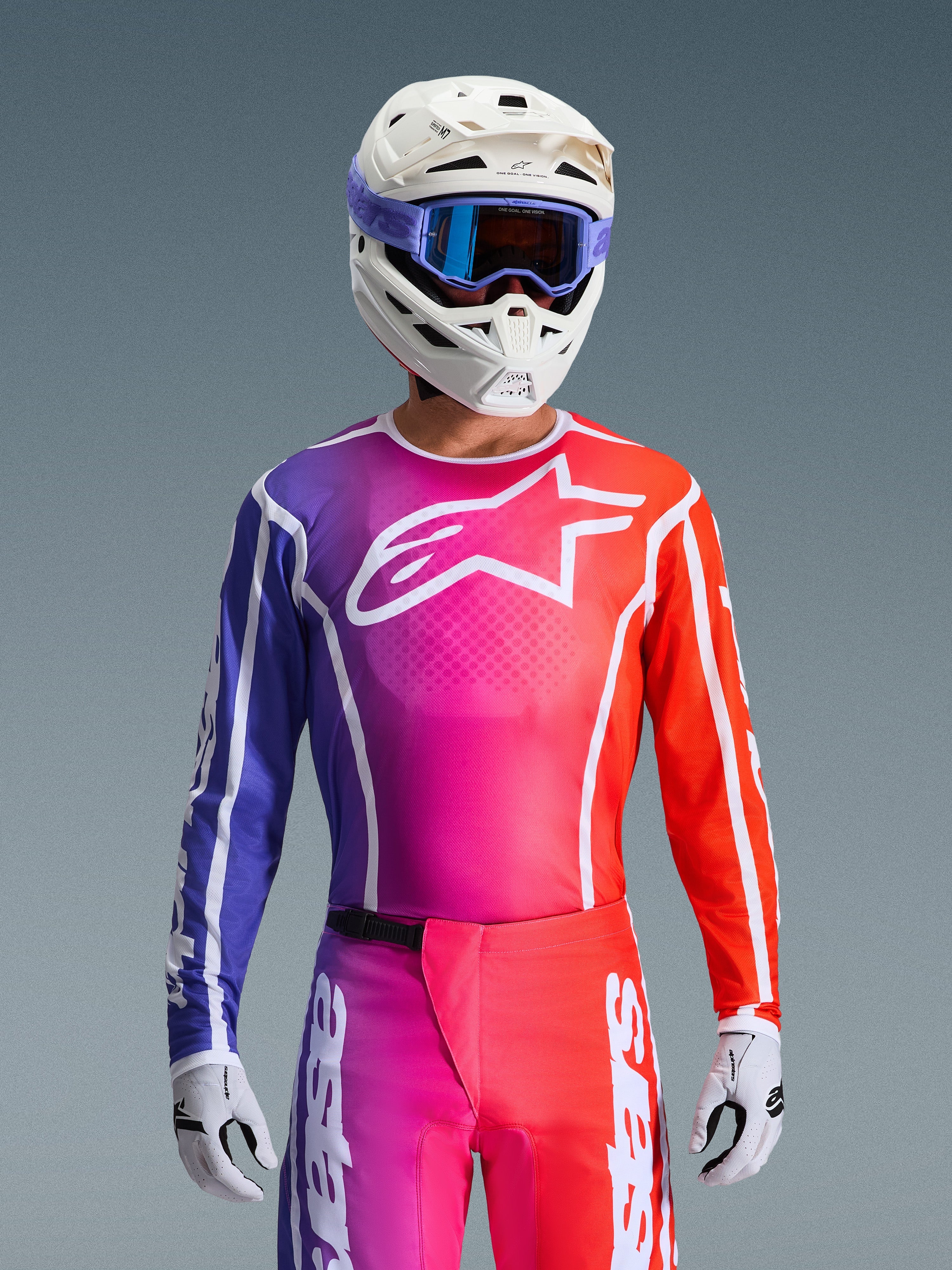 Alpinestars 2026 Fluid Apex utrustningsset, motocrosströja och byxor med en gradientdesign i lila, rosa och orange, vit Alpinestars stjärnlogotyp på bröstet, vit hjälm och lila goggles, högpresterande atletisk passform för terrängkörning