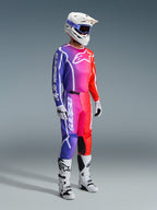 Motocrossförare i komplett racingutrustning, 2026 Fluid Apex-tröja och byxor med en livfull gradient i lila, rosa och orange, vit hjälm med blå goggles, vita och svarta stövlar och vita handskar, koordinerad outfit för motocross.