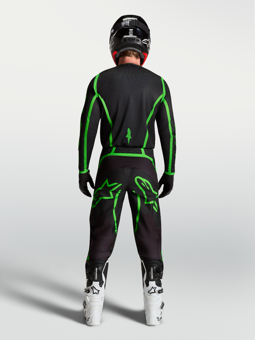Alpinestars Fluid Apex V2 byxor, svarta och gröna motocrossbyxor sedda bakifrån på en förare med vita stövlar.