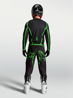 Alpinestars Fluid Apex V2 byxor, svarta och gröna motocrossbyxor sedda bakifrån på en förare med vita stövlar.
