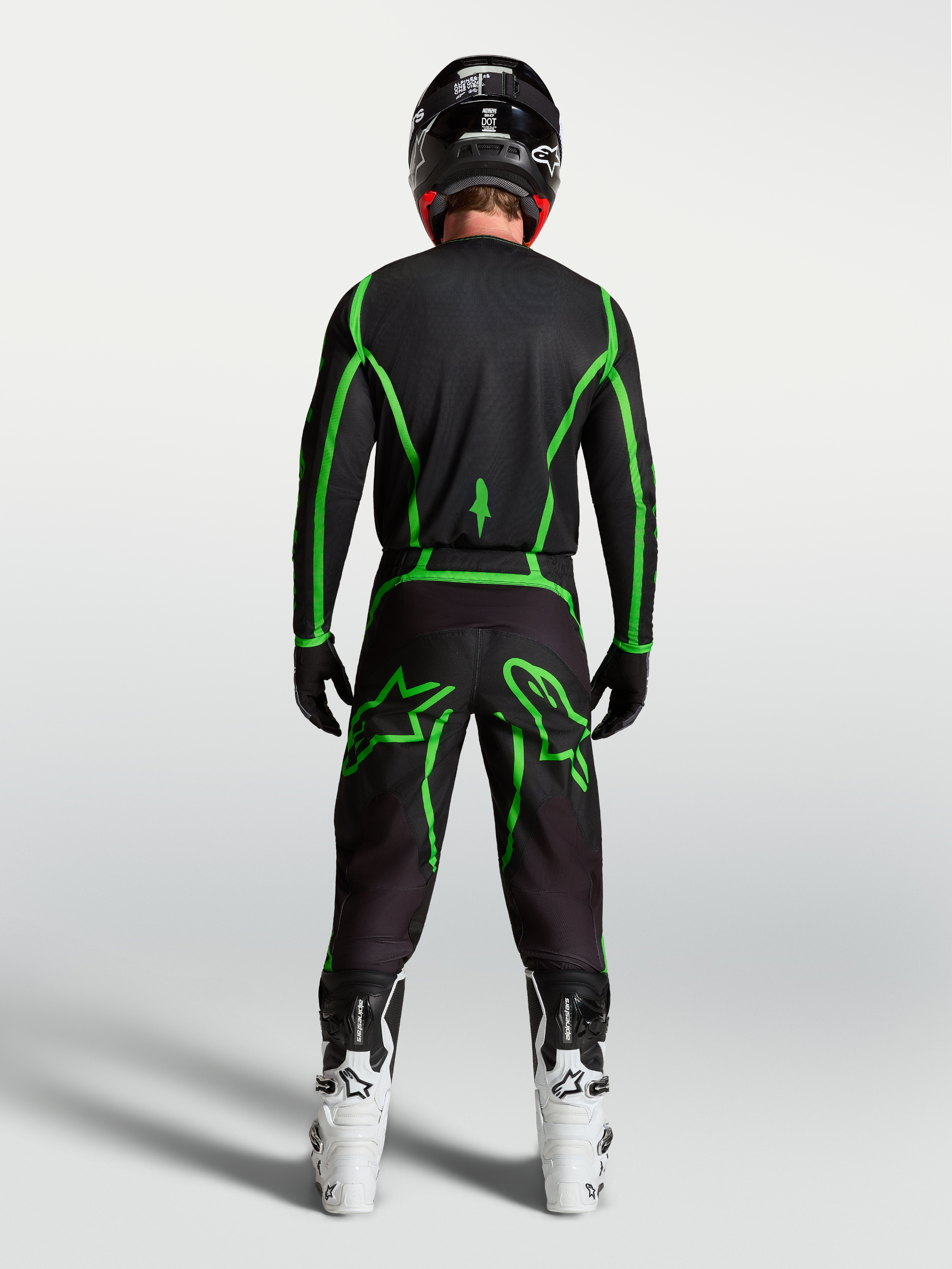 Alpinestars Fluid Apex V2 byxor, svarta och gröna motocrossbyxor sedda bakifrån på en förare med vita stövlar.