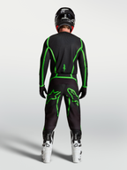 Alpinestars Fluid Apex V2 tröja, motocrossutrustning, svart och neongrön, vy bakifrån på förare med vita MC-stövlar.