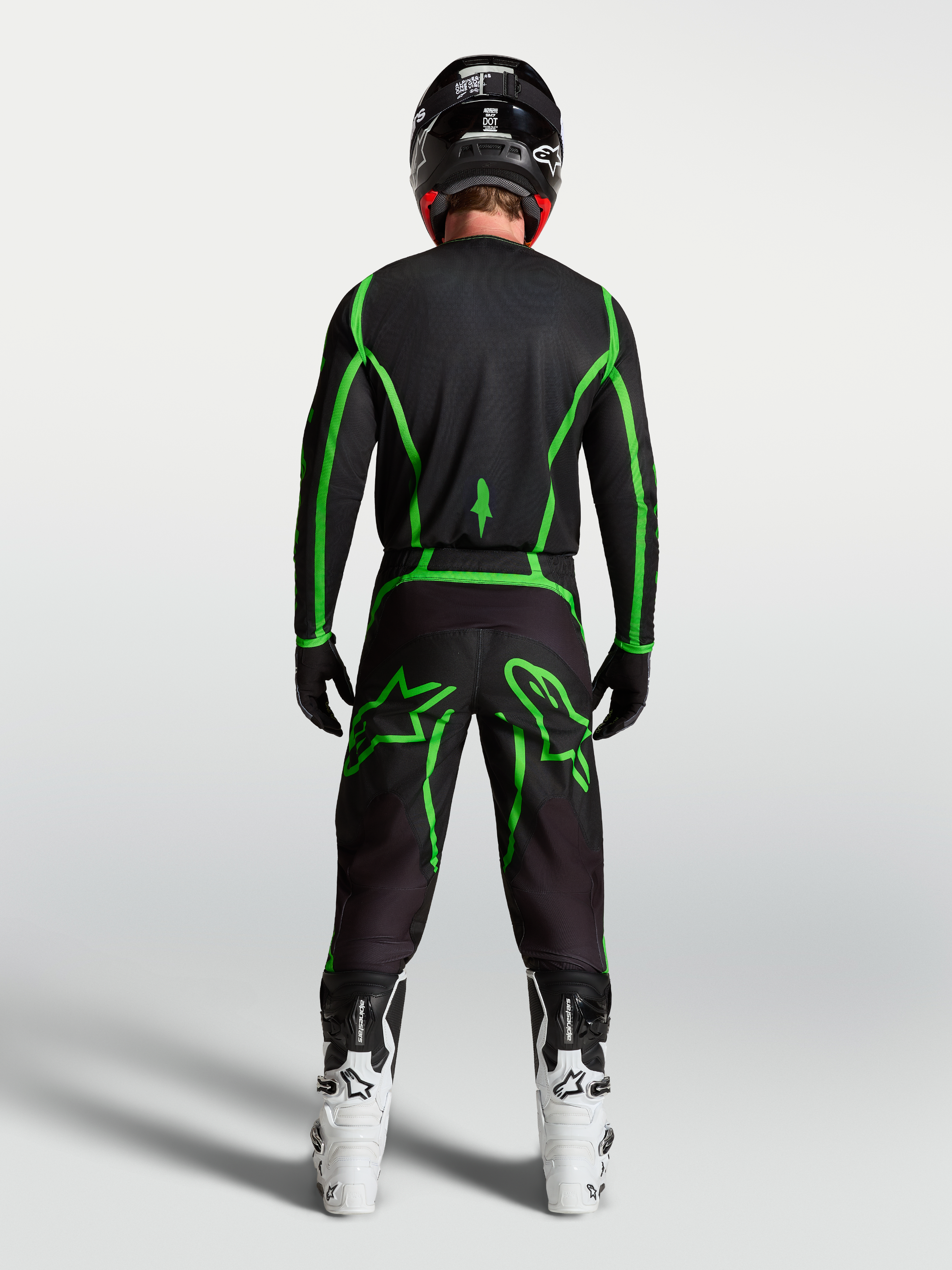 Alpinestars Fluid Apex V2 tröja, motocrossutrustning, svart och neongrön, vy bakifrån på förare med vita MC-stövlar.