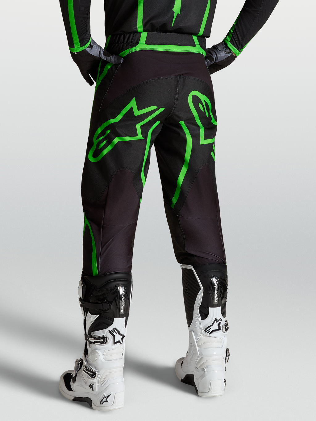 Alpinestars Fluid Apex V2 byxor, motocrossbyxor herr i svart och grön fluo, vy bakifrån på modell med vita off-road-stövlar.