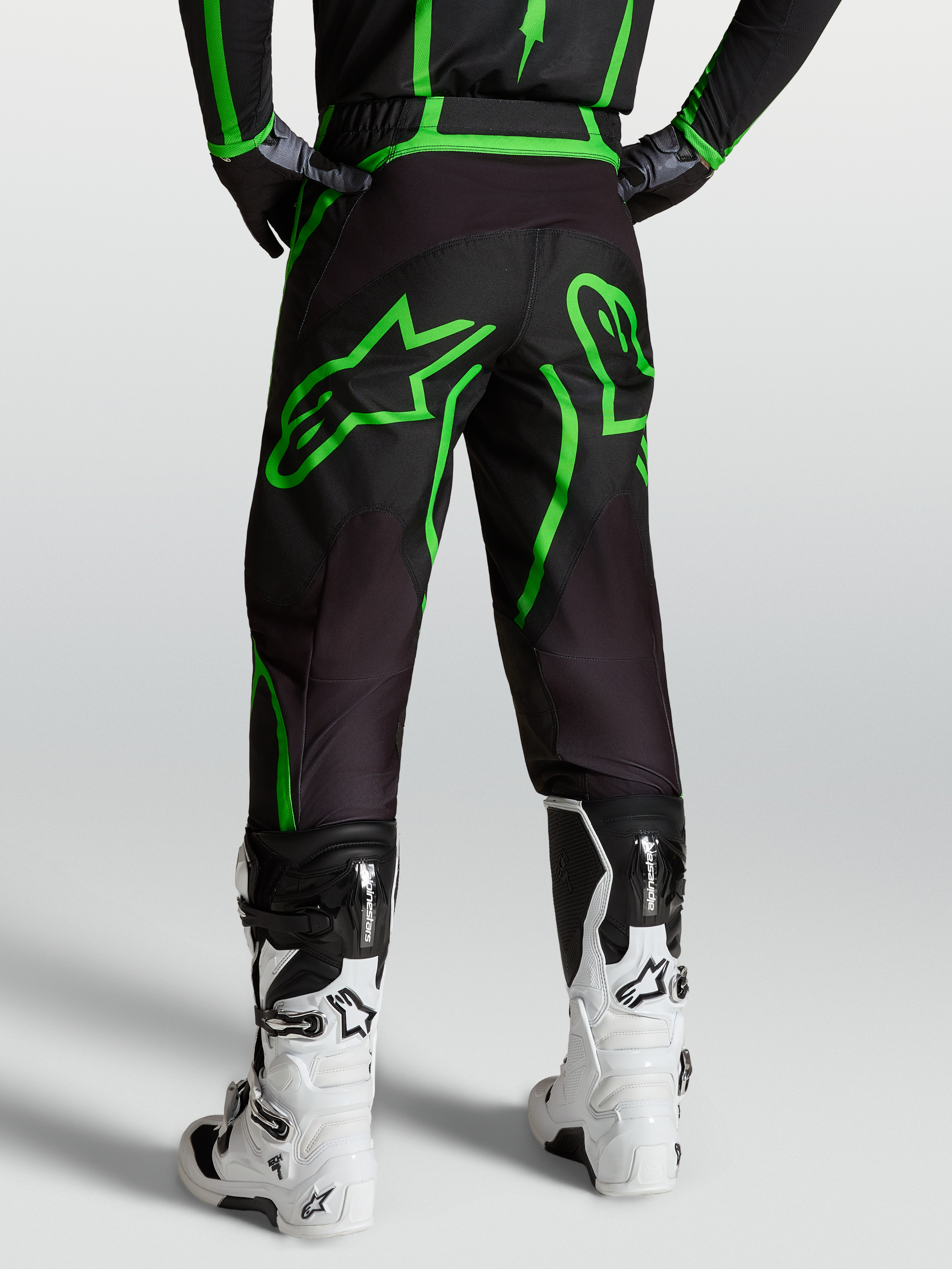 Alpinestars Fluid Apex V2 byxor, motocrossbyxor herr i svart och grön fluo, vy bakifrån på modell med vita off-road-stövlar.