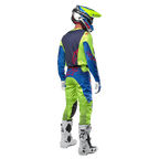 Motocrossförare sedd bakifrån i Alpinestars 2024 Racer Hoen-tröja i Yellow Fluo och Blue Night Navy, matchande motocrossbyxor och vita stövlar, visar ryggdesignen med röda logotyper, koordinerad outfit för professionell terrängkörning