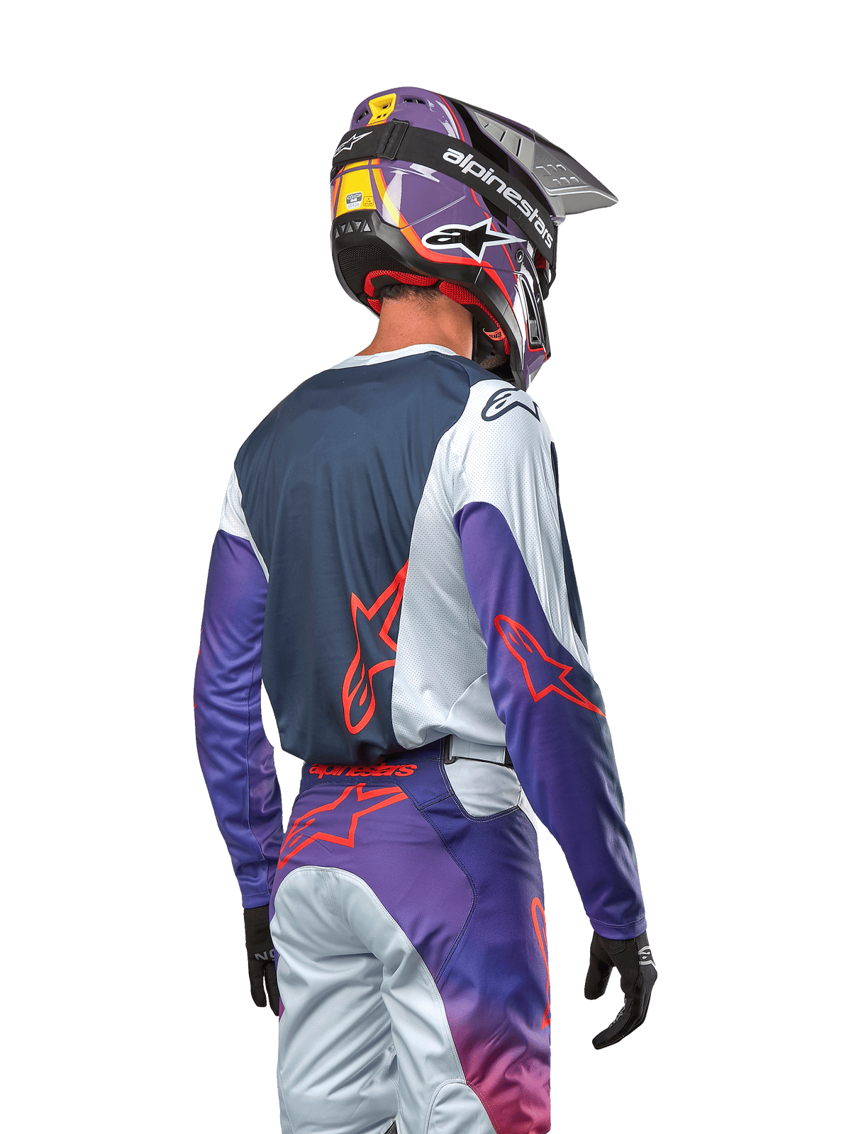 Motocrossförare sedd bakifrån bärande 2024 Racer Hoen Jersey, marinblå ryggpanel med ljusgrå axlar och lila ärmar, Alpinestars-logotyper i hot orange, matchande lila och grå byxor med en lila motocrosshjälm, komplett outfit för terrängkörning