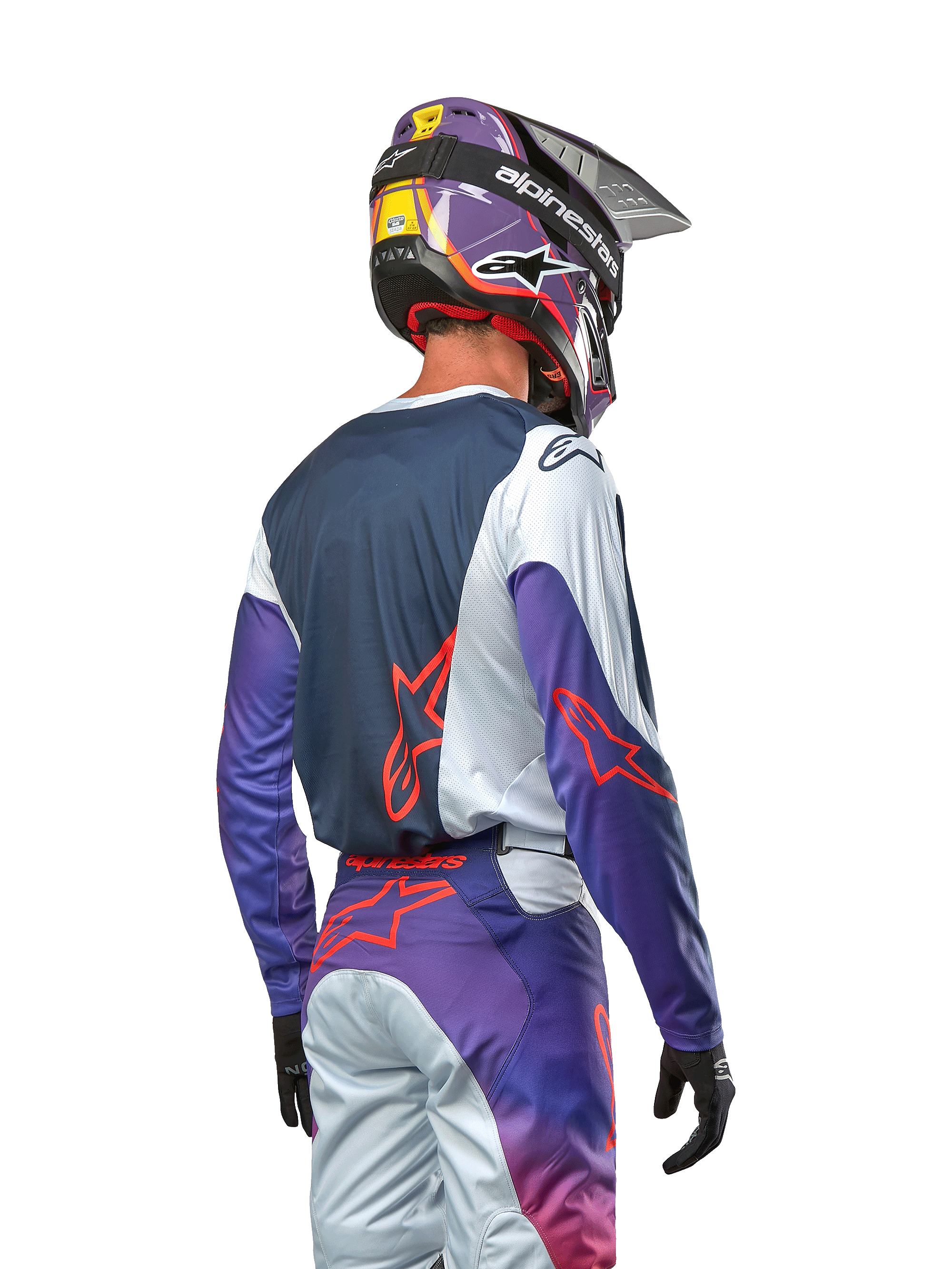Motocrossförare sedd bakifrån bärande 2024 Racer Hoen Jersey, marinblå ryggpanel med ljusgrå axlar och lila ärmar, Alpinestars-logotyper i hot orange, matchande lila och grå byxor med en lila motocrosshjälm, komplett outfit för terrängkörning