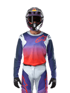Alpinestars 2024 Racer Hoen Jersey i ljusgrå, stark orange och svart, motocrosströja som bärs av en förare med matchande utrustning, med en livfull färggradient och Alpinestars stjärnlogotyp på bröstet, designad för offroad-prestanda.