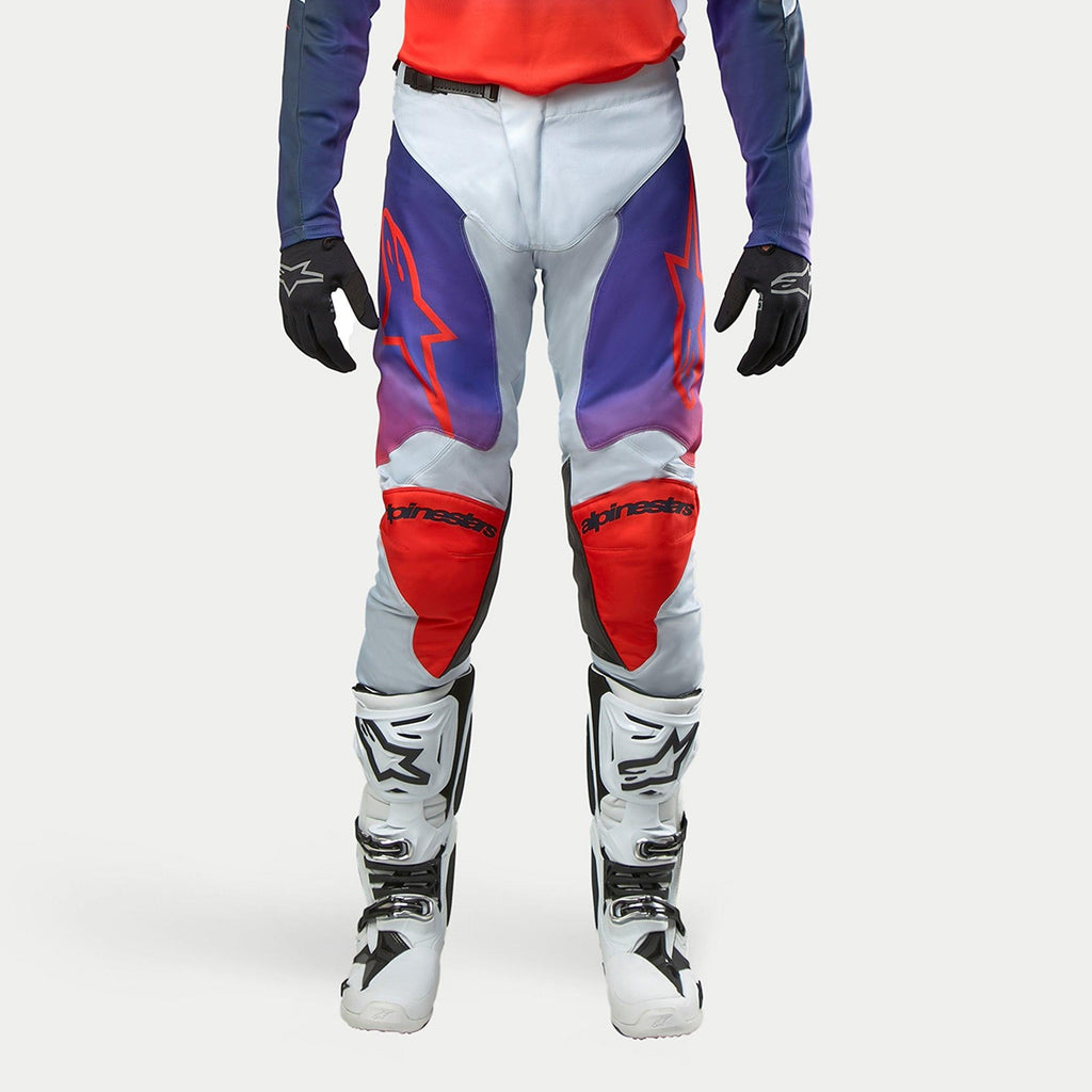 Alpinestars 2024 Racer Hoen byxor, motocrossbyxor i ljusgrått med lila och röda grafiska detaljer, röda logotyper på lår och knän, vita motocross-stövlar, svarta handskar, professionell racingutrustning för terrängkörning