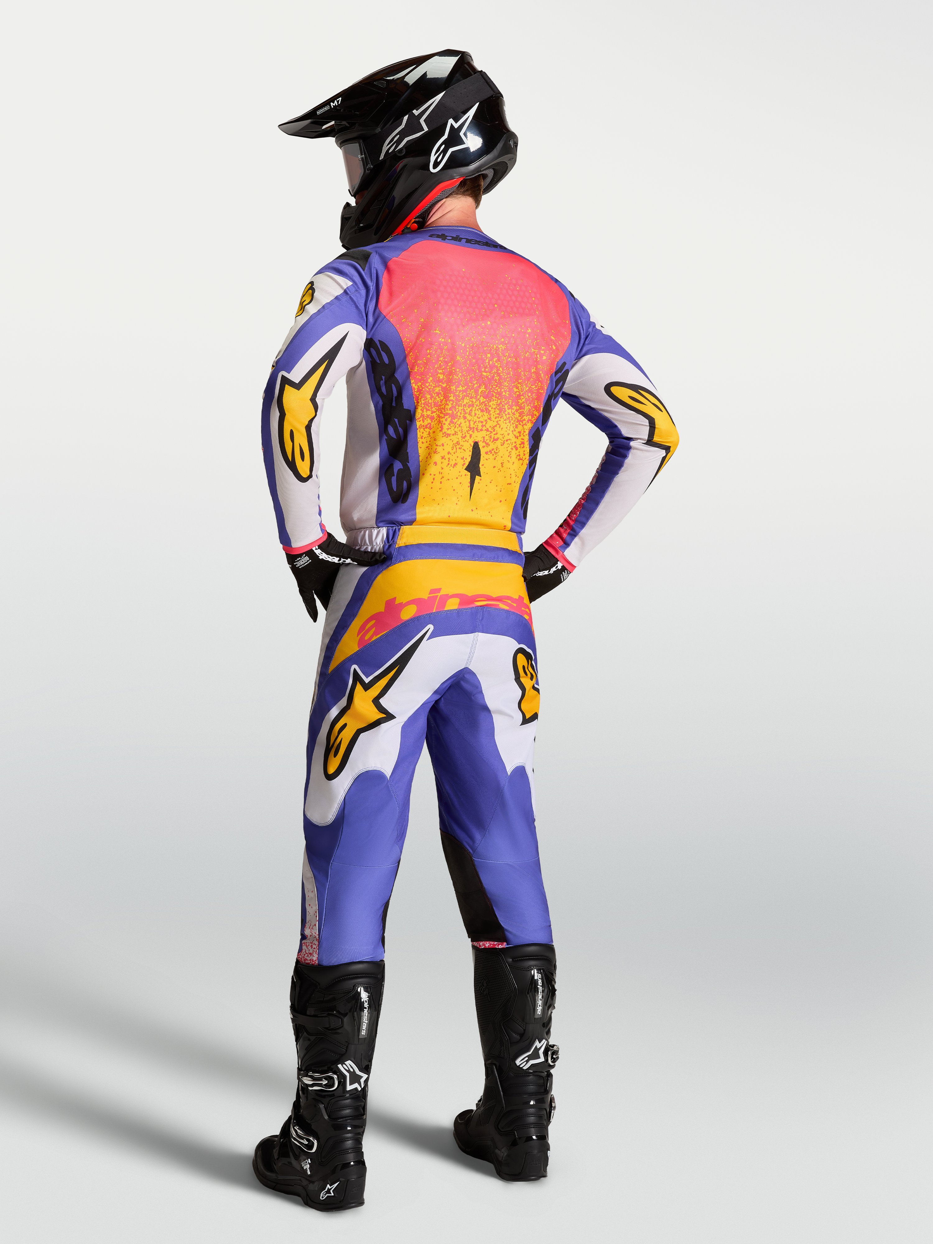 Alpinestars Fluid Drag klädset, motocrosströja och byxor för herrar, blå och lila med iris gold, vy bakifrån på förare.