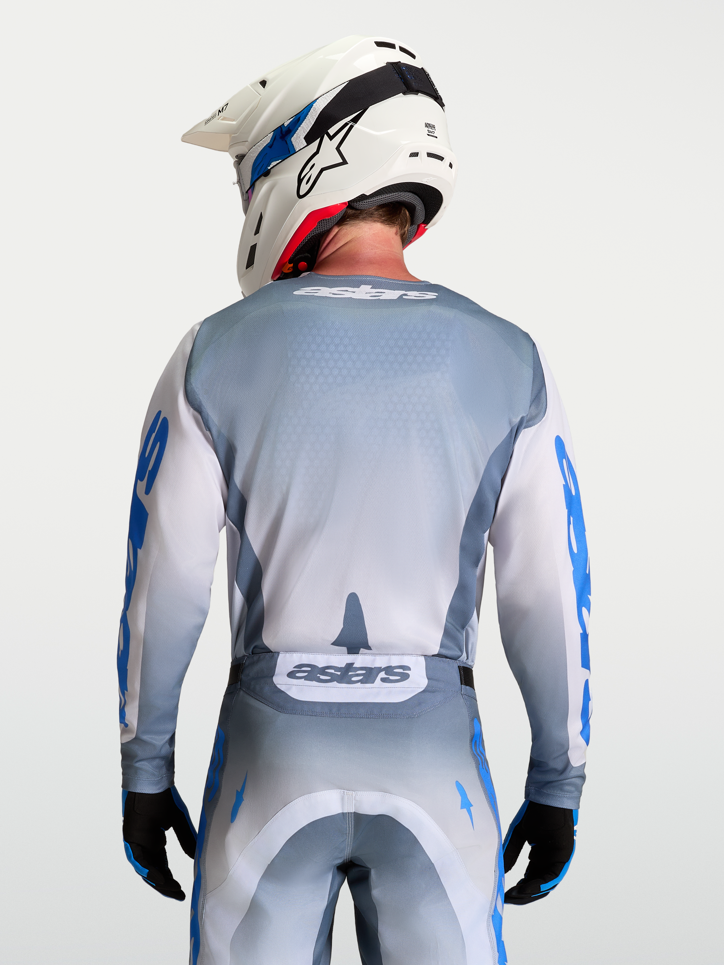 Alpinestars Racer Amber Jersey, Gray and White Motocross Jersey, Ash Gray moisture-wicking polyfabric with light lilac and UCLA blue graphics, ergonomic race fit, on-model rear view with white helmet.
